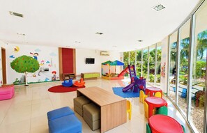 Une salle de jeux pour enfants avec un espace de jeu, des sièges et une grande fenêtre.