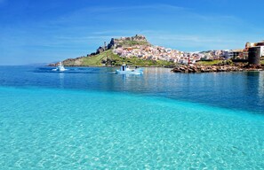 A coastal town with clear blue waters, a boat, and a hilltop castle.
