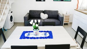 Ein modernes Wohnzimmer mit Esstisch, grauem Sofa und einer Waschmaschine im Hintergrund.