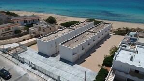 Ein modernes Gebäude mit flachem Dach und mehreren Balkonen, direkt neben einem Strand.