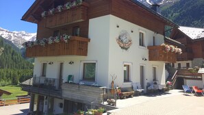 A two-story wooden building with balconies adorned with flowers, a mountain view, and a sign indicating a location in Buchenwald. - TWO-ROOM RELAX SPA SKI AND TREKKING IN THE ALPS (Santa Caterina)