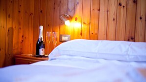 A wooden-paneled room with a bed, a bottle of champagne, and two glasses on a nightstand. - TWO-ROOM RELAX SPA SKI AND TREKKING IN THE ALPS (Santa Caterina)