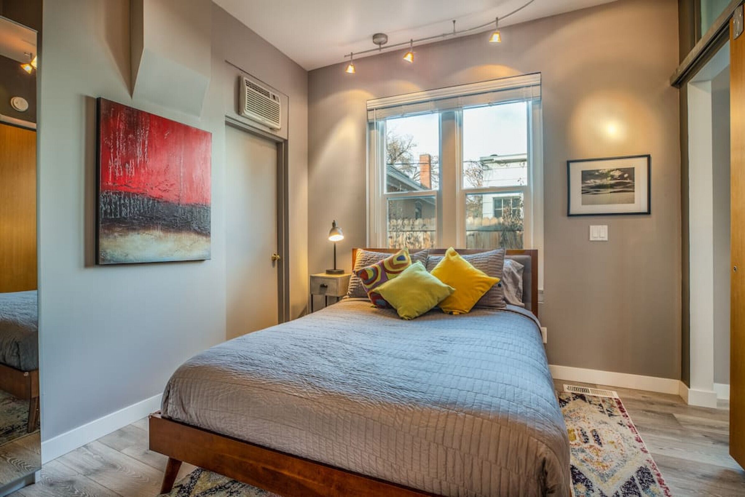 A bedroom with a large bed, a window with a view, and a painting on the wall.