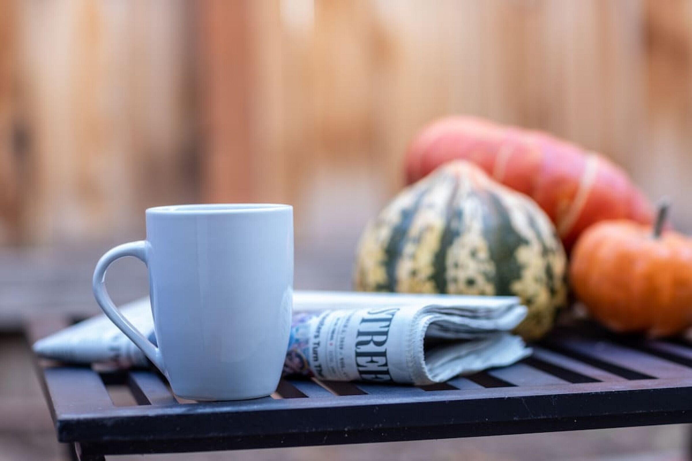 A table with a white mug, a folded newspaper, and two pumpkins.