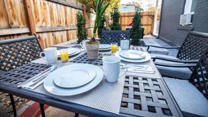 Eine Terrasse im Freien mit einem für das Frühstück gedeckten Tisch, einschließlich Tellern, Tassen und einer Karaffe Orangensaft.