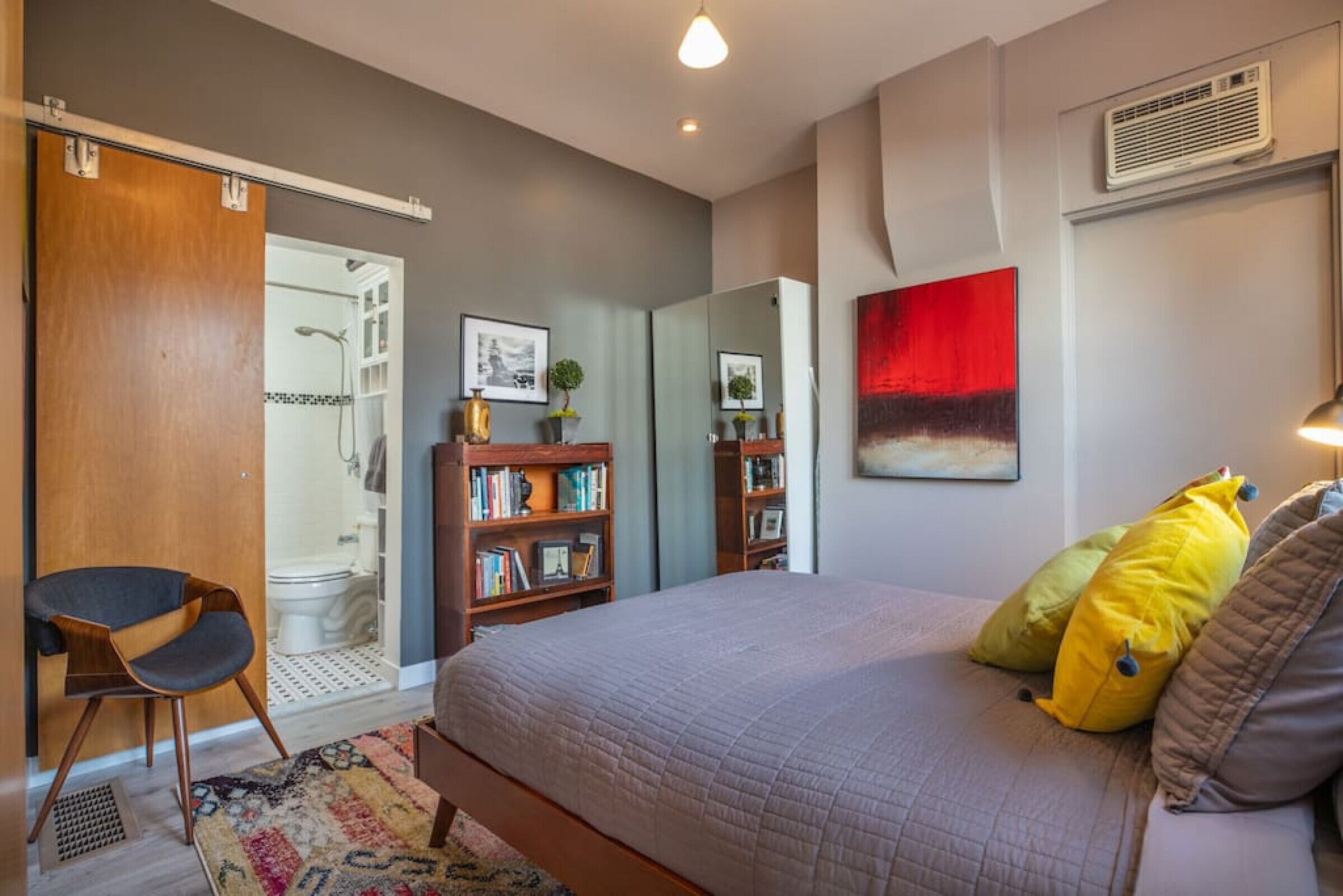 A bedroom with a bed, a bookshelf, a chair, and a shower area.