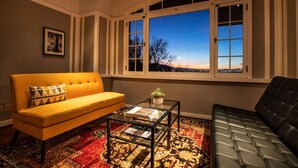 A living room with a yellow sofa, a black sofa, a glass coffee table, and a view of the sunset through a bay window. - Stunning View, Frank Lloyd Wright Inspired Home (Salt Lake City)