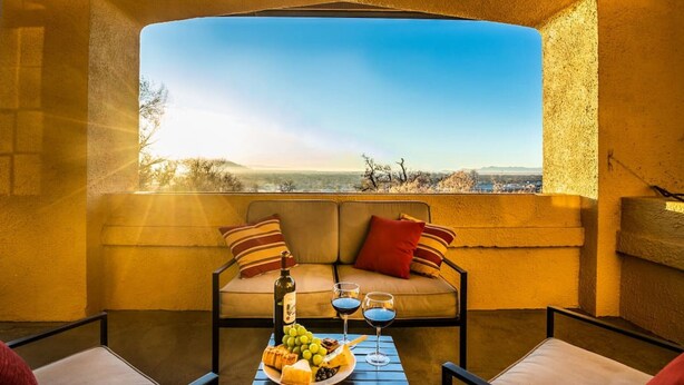 A cozy seating area with a sofa and armchairs, a table with a bottle, glasses, and snacks, and a scenic view through a large window. - Stunning View, Frank Lloyd Wright Inspired Home (Salt Lake City)