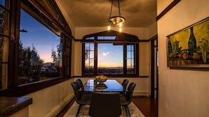 A dining area with a glass table, black chairs, a fruit bowl, and a view of the sunset through large windows. - Stunning View, Frank Lloyd Wright Inspired Home (Salt Lake City)