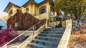 Una casa de dos pisos con una escalera de piedra que lleva a la puerta principal, rodeada de follaje otoñal y un cielo azul despejado.