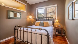 Un dormitorio con estructura de cama metálica, un espejo grande, una ventana con vistas y una mesita de noche con lámpara.