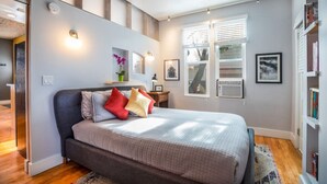 A bedroom with a bed, a nightstand, a window with blinds, and a bookshelf. - New distinctive historical  unit from 5 Star Host (Salt Lake City)
