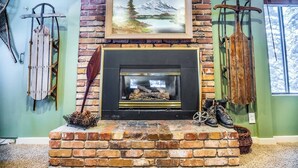 Una chimenea con un cuadro enmarcado encima, esquíes apoyados contra la pared y un cesto de piñas sobre el hogar.