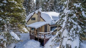 Una cabaña nevada con terraza de madera y chimenea.
