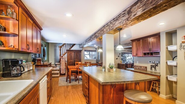 Una cocina con armarios de madera, una isla central y una zona de comedor con una escalera que sube a una buhardilla.