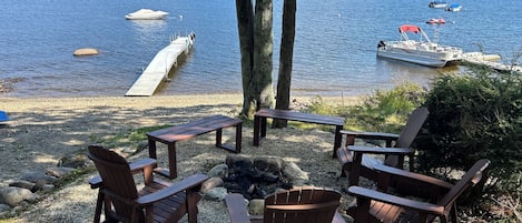 Relax on the lakeside deck with Adirondack chairs and a fire pit, surrounded by a lush hill and access to boating.