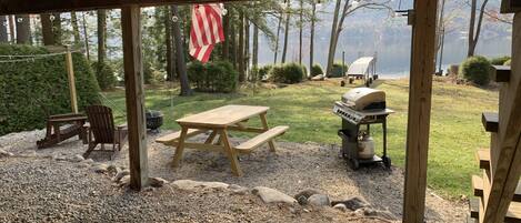 A covered outdoor area with a picnic table, grill, and seating.