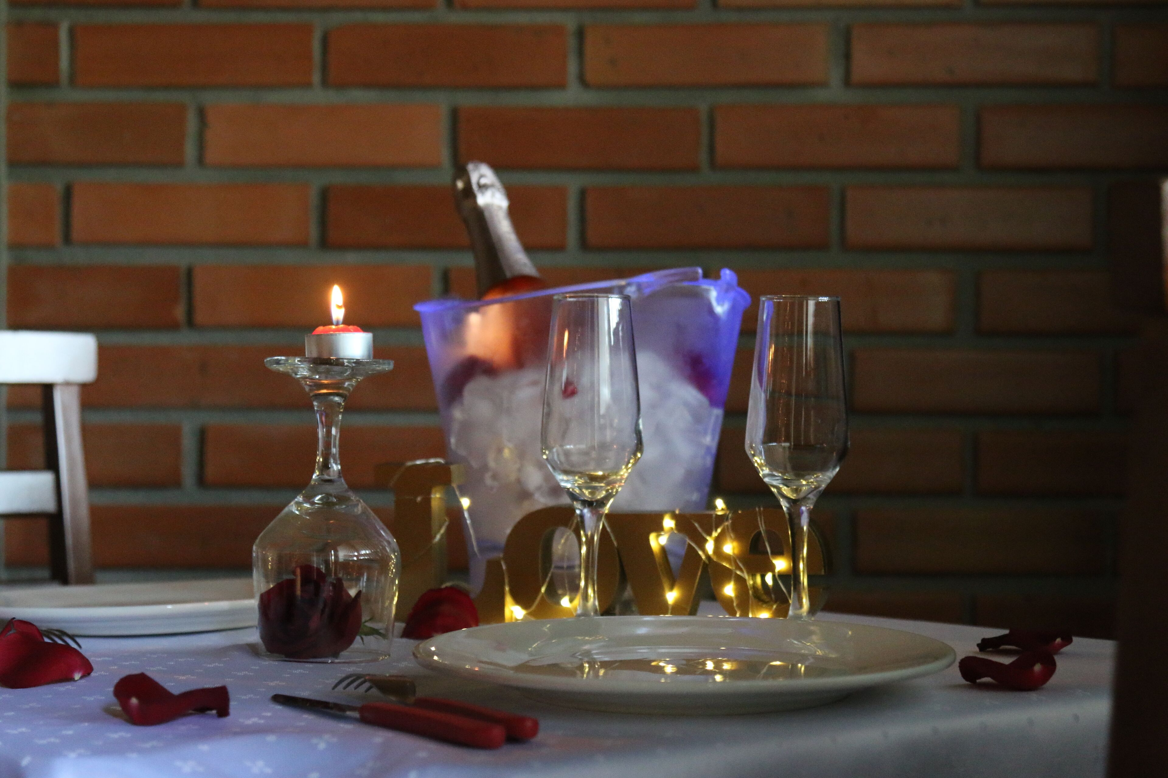 Una mesa dispuesta con una vela, copas de vino y un cuenco de vidrio con una rosa.