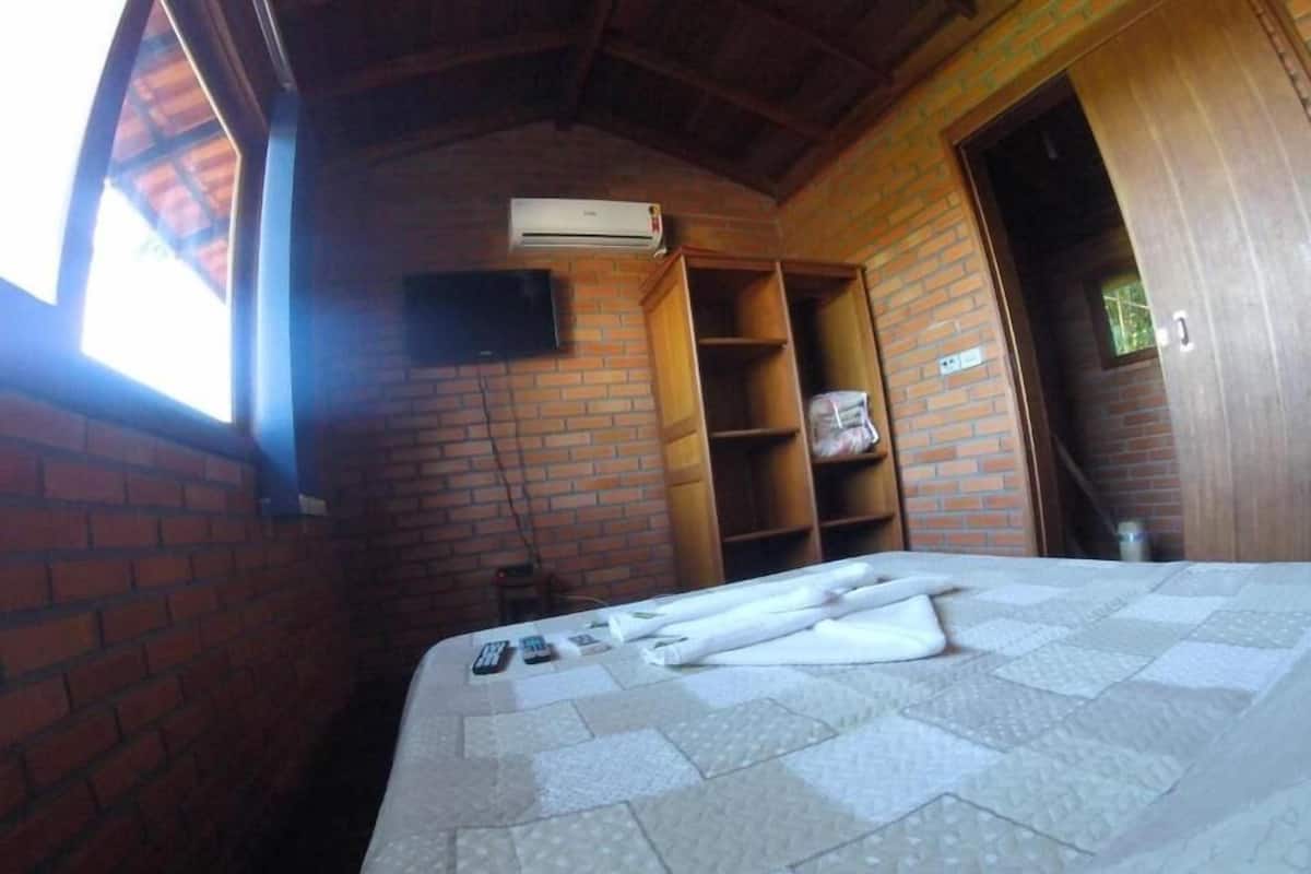 A room with a brick wall, a bed with a quilt, an air conditioning unit, and a wooden door.
