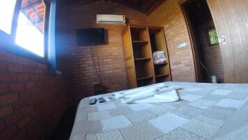 A room with a brick wall, a bed with a quilt, an air conditioning unit, and a wooden door.