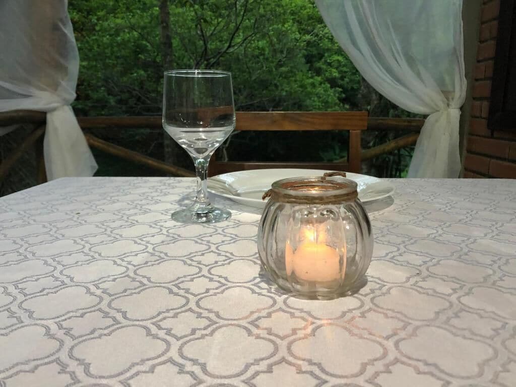 A table with a candle in a glass jar, a wine glass, and a plate.