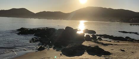 Una playa con rocas y agua tranquila, cielo despejado y colinas a lo lejos.