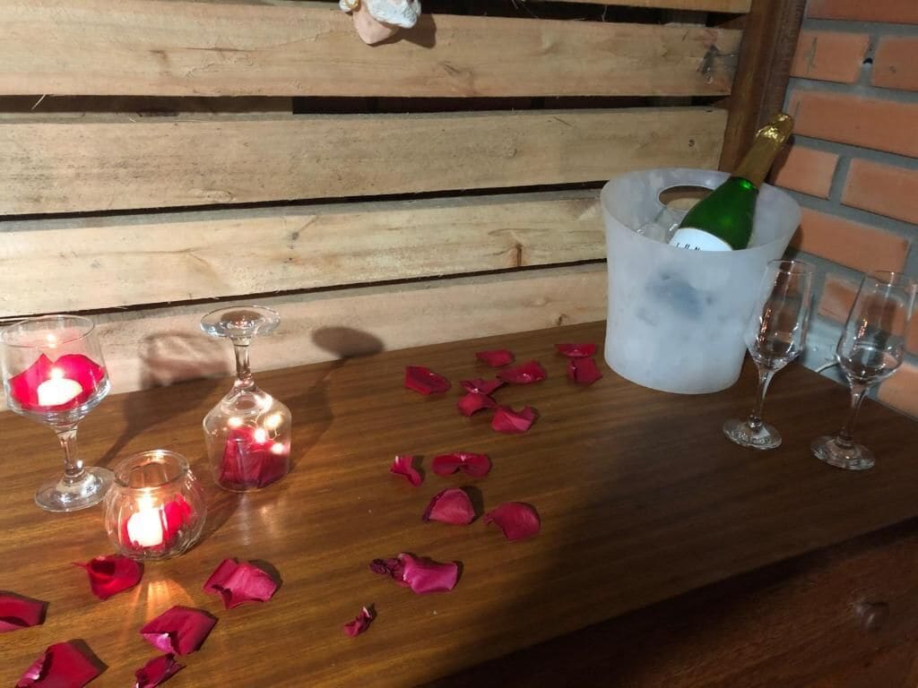 Una mesa de madera con una botella de champán en un balde de hielo, rodeada de copas y pétalos de rosa dispersos.