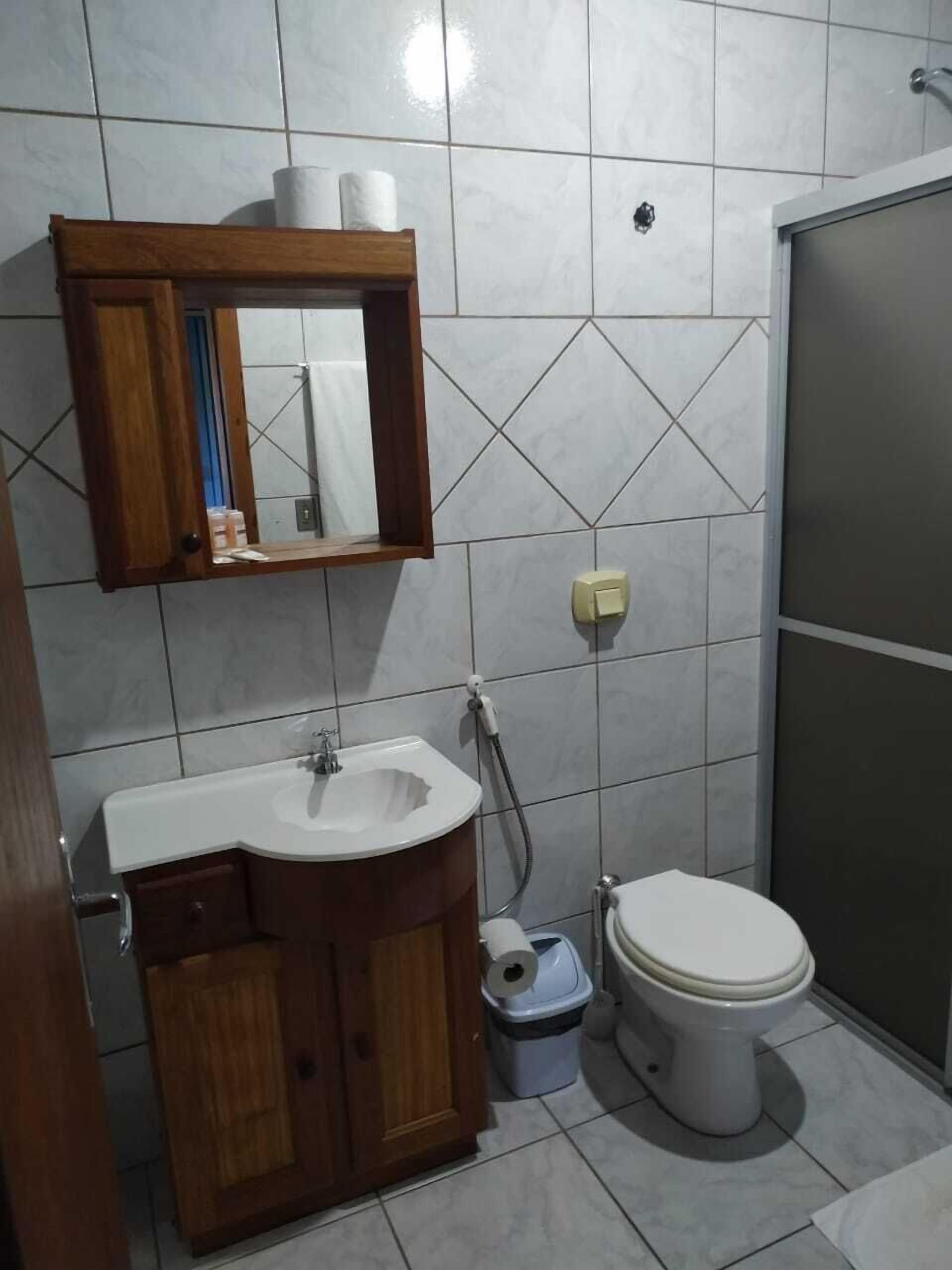 Une salle de bain avec un meuble-lavabo en bois, un lavabo blanc, des toilettes et un espace douche.