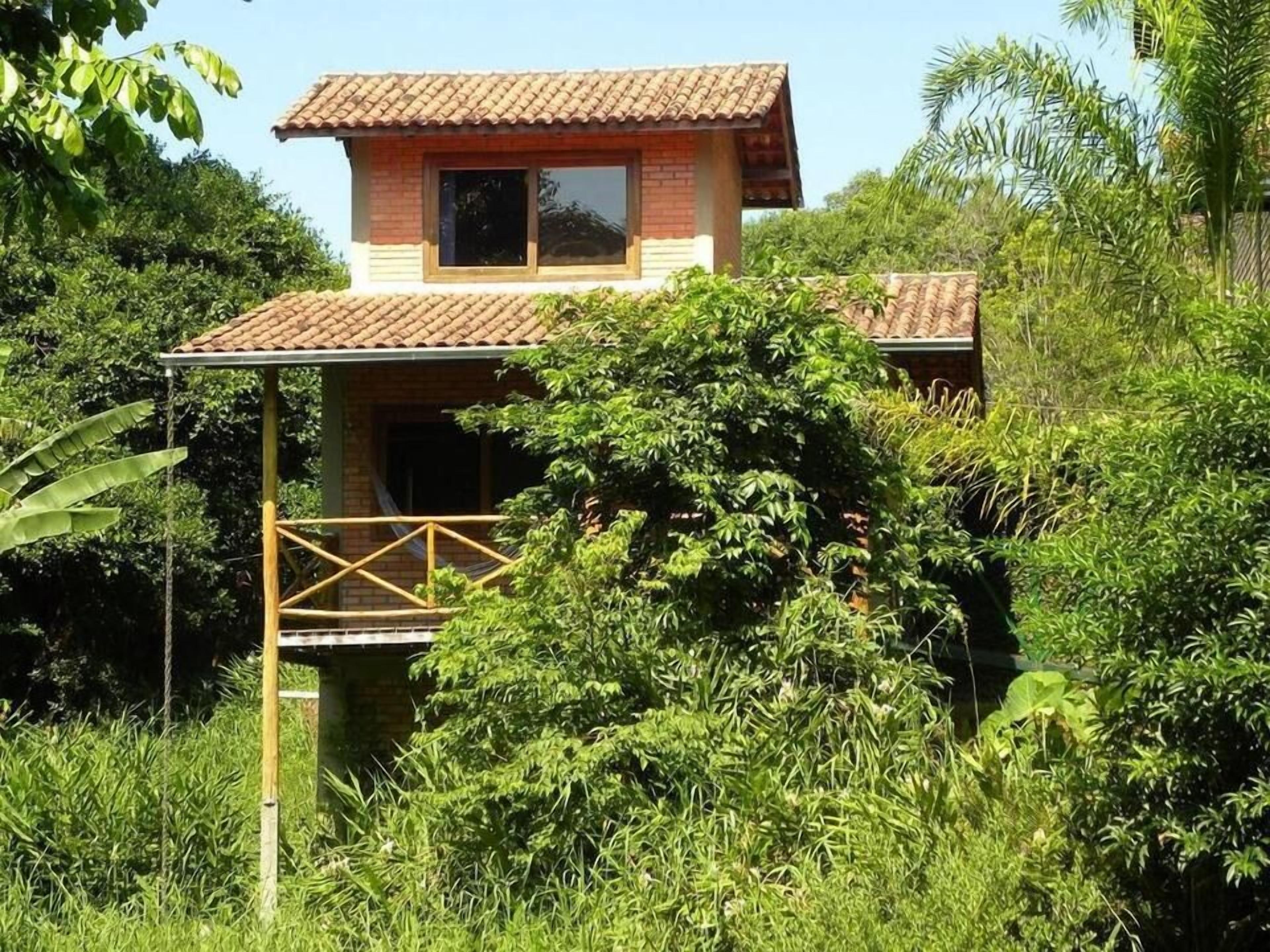 Una casa de dos pisos con techo de tejas, rodeada de abundante follaje.