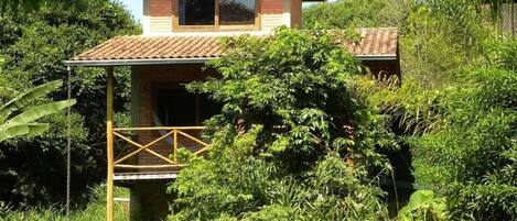 Una casa de dos pisos con techo de tejas, rodeada de abundante follaje.