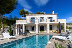 Une maison à deux étages avec une piscine, un espace salon extérieur et une vue sur le paysage environnant.