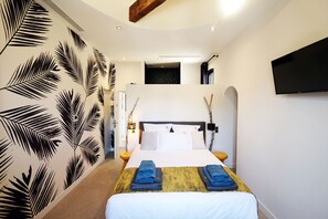 Une chambre d’hôtel moderne dotée d’un grand lit, d’un téléviseur à écran plat et d’un mur décoratif orné de motifs de feuilles de palmier.
