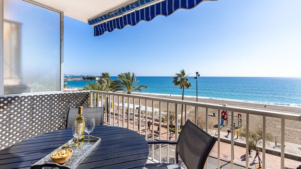 Ein Balkon mit Tisch, Stühlen und einer Weinflasche. Blick auf Strand und Meer.