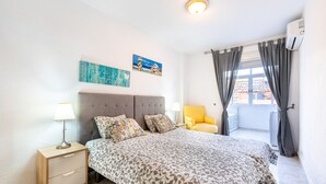 Ein Schlafzimmer mit Bett, Nachttischen, einem Fenster mit Vorhängen und Wandbildern.