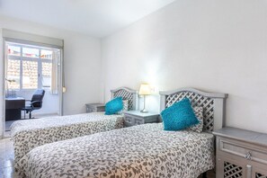 A hotel room with two beds, a desk, a chair, and a window with curtains. - Maritimo Fuengirola | Lovely Beachfront Apartment with Panoramic Sea Views in Fuengirola (Fuengirola)