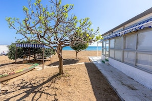 A beachside property with a covered seating area, a tree, and a building with large windows. - Maritimo Fuengirola | Lovely Beachfront Apartment with Panoramic Sea Views in Fuengirola (Fuengirola)
