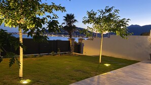 Un jardin avec une terrasse en bois, une pelouse et un mur en pierre.