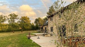 A stone building with a patio area, surrounded by a grassy lawn and trees. - La Chouette (Nouziers)