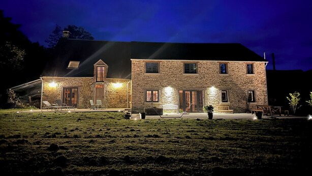 A stone building with a large front porch and multiple windows, illuminated by exterior lights. - La Chouette (Nouziers)