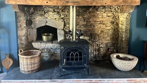 A stone fireplace with a black wood stove, a metal pot, and two baskets. - La Chouette (Nouziers)