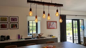 A modern kitchen with a central island, pendant lighting, and a dining area with a view of the outdoors. - La Chouette (Nouziers)