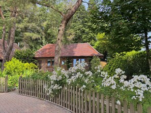 Ein Haus aus Ziegelsteinen mit rotem Dach, umgeben von üppigem Grün und weißen Blütenpflanzen.