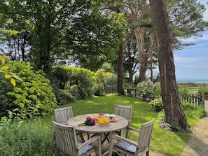 A round wooden table with chairs, a bouquet of flowers, and a plate of fruit and a glass of orange juice.
