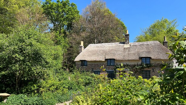Une maison traditionnelle à toit de chaume, entourée d’une végétation luxuriante et bordée d’un chemin de gravier.