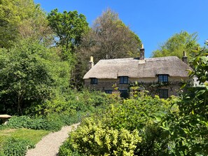 Een huis met rieten dak, omringd door weelderige begroeiing en een grindpad.
