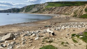 Une plage côtière avec un terrain rocheux, un bateau sur l’eau et des falaises en arrière-plan.