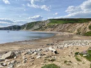 A coastal beach with rocky terrain, a boat in the water, and cliffs in the background.
