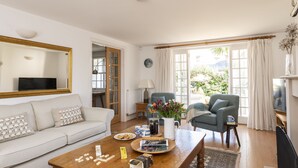 Un salon comprenant un canapé, une table basse et des fauteuils, un téléviseur et une fenêtre avec des rideaux.