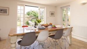 Une cuisine lumineuse avec une table en bois, trois chaises et une vue sur le jardin grâce à de grandes fenêtres.
