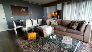 Een moderne woonkamer met een bruine bank, een glazen salontafel, en een eethoek met gestreepte stoelen en een kandelaar.